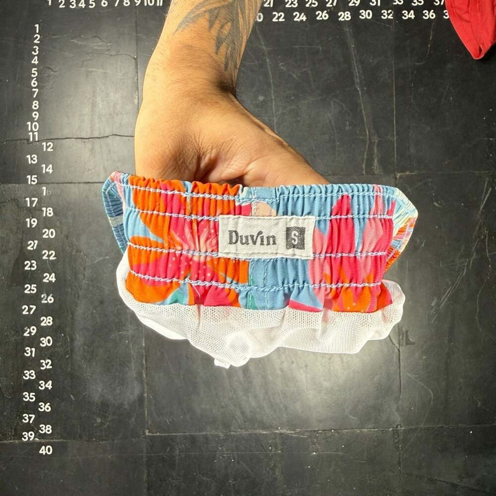 The Room Collective Duvin Design floral print swim trunks in light blue with pink and orange hibiscus, size small. Features elastic waistband and mesh lining.