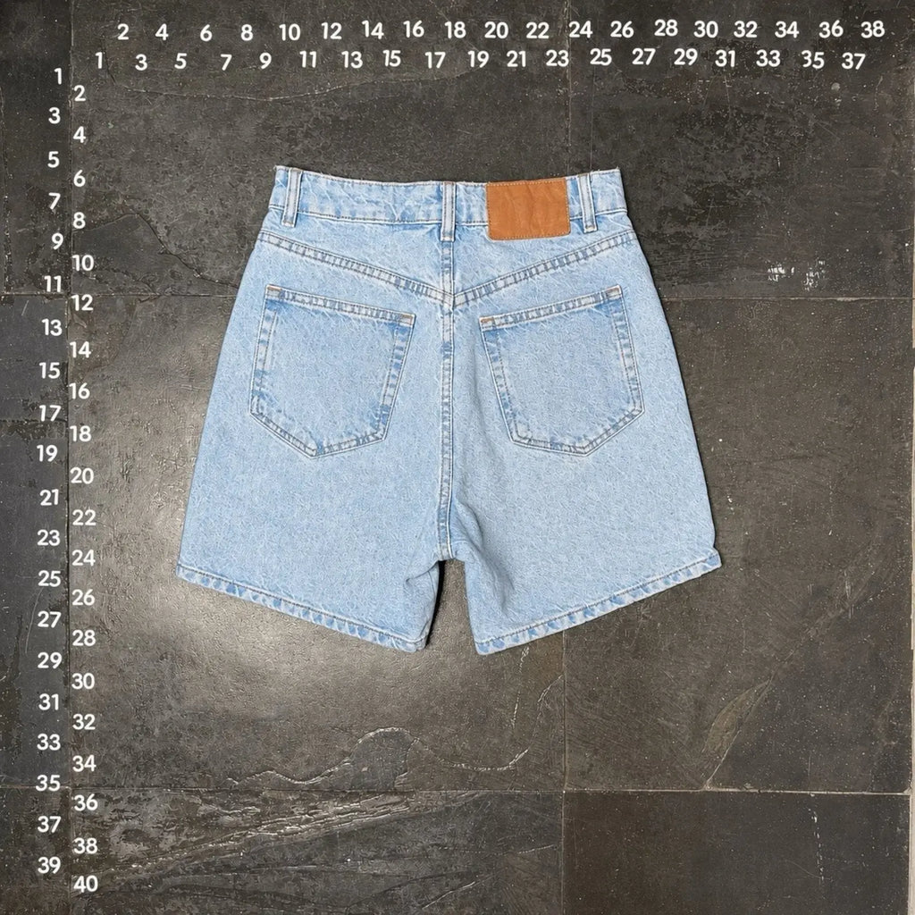 The Room Collective light wash denim shorts with five-pocket styling and a brown leather patch.