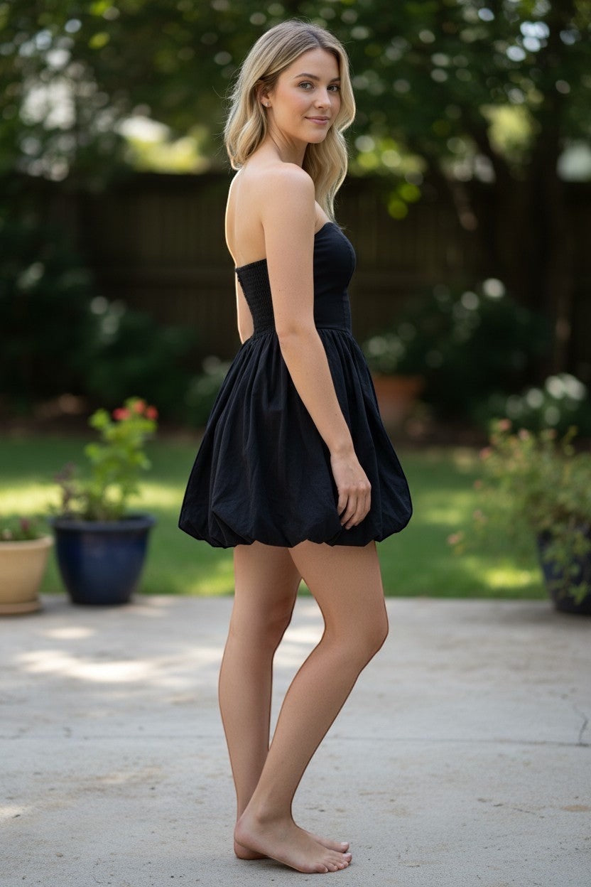 The Room Collective black strapless sweetheart mini dress with shirred back and bubble hem skirt. Model is wearing a size Medium.