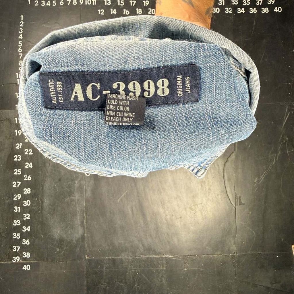 The Room Collective AC-3998 light wash denim trucker jacket with distressed details and "Est. 1998" tag.