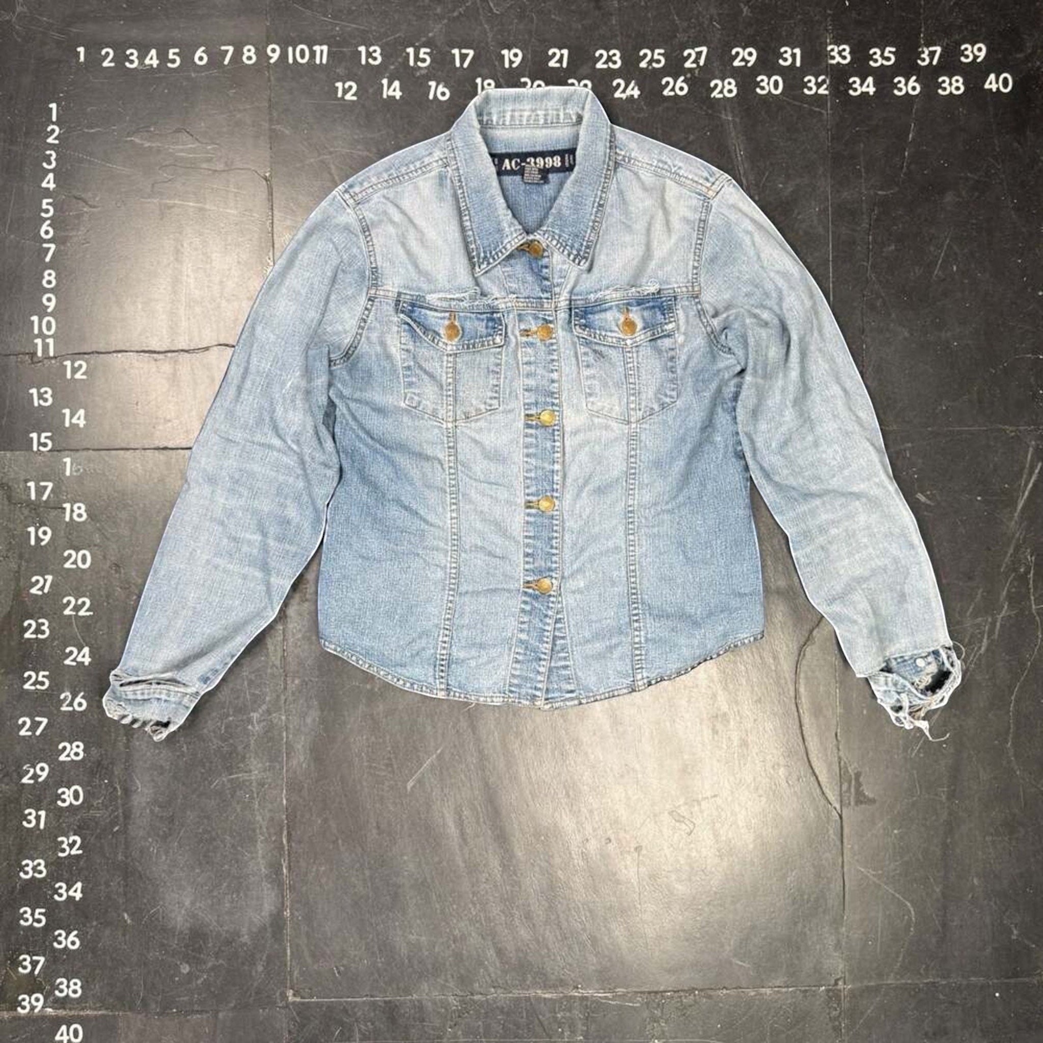 The Room Collective AC-3998 light wash denim trucker jacket with distressed cuffs and hem, gold-tone buttons, and dual chest pockets.