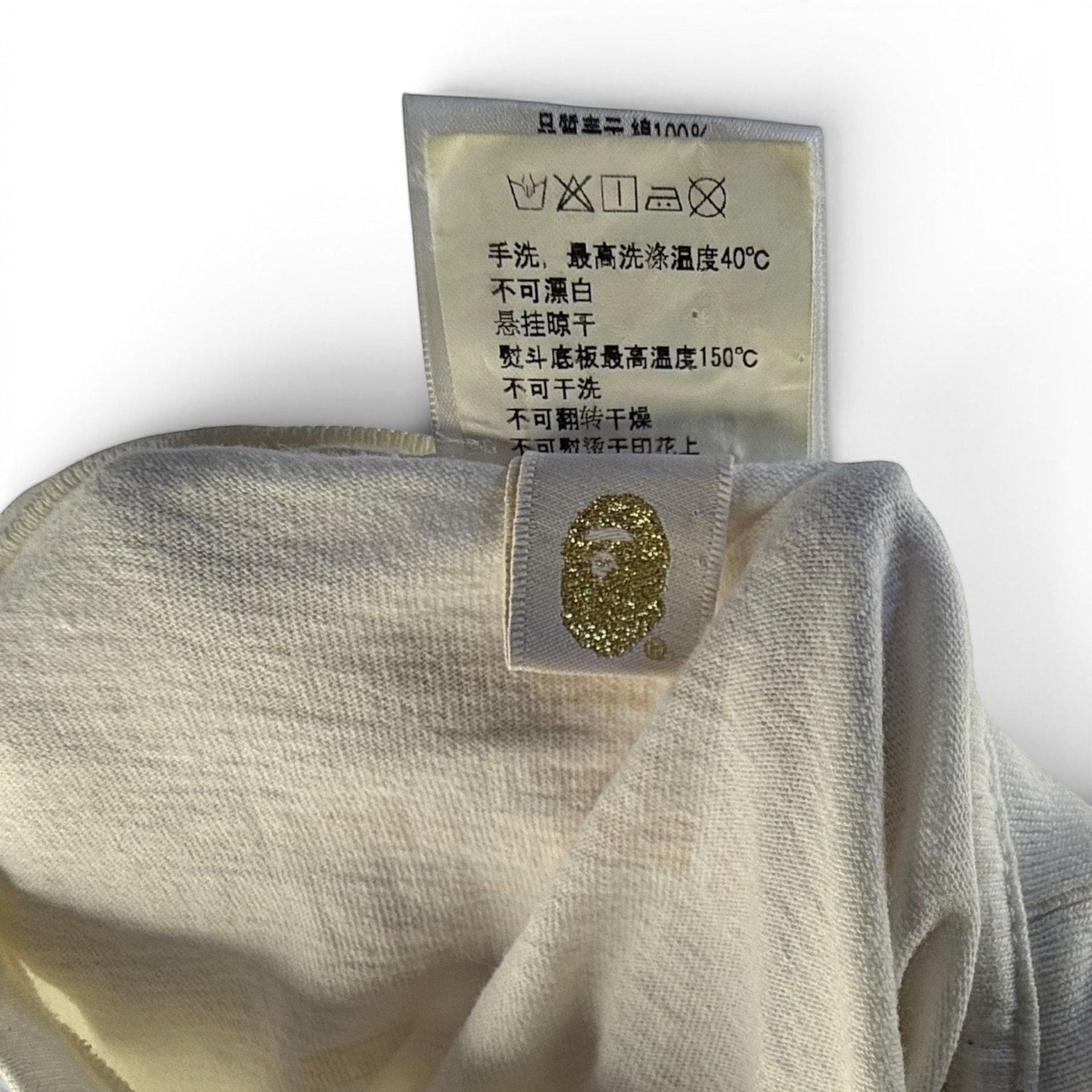 The Room Collective white 100% cotton A Bathing Ape t-shirt with gold ape head logo and tiger camo detail.